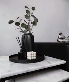 a black vase with some white balls on top of it sitting on a marble table