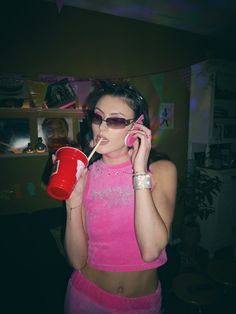 a woman in pink talking on a cell phone and drinking from a red cup while holding a straw