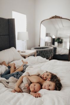 two young children laying on top of each other on a white bed in a bedroom