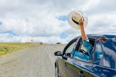 a person with a hat on their head leaning out the window of a blue car