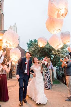 a bride and groom are walking through the street with paper lanterns in the air above them