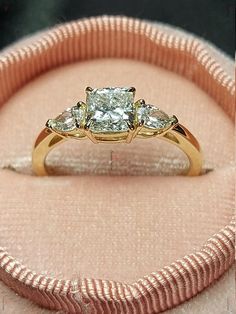 three stone diamond ring sitting on top of a pink velvet cushioned box with ribbon around it