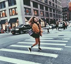 a woman is crossing the street with her hair blowing in the wind while wearing a fur coat