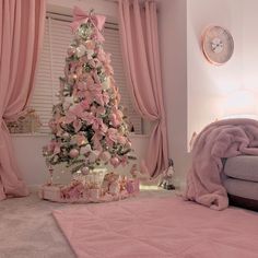 a pink christmas tree in the corner of a room with curtains and blankets on it