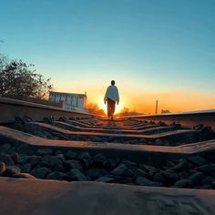 a man standing on top of train tracks at sunset