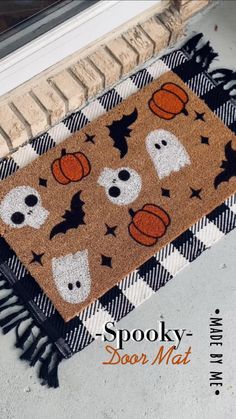 a halloween door mat with pumpkins and ghost faces on it, next to a window