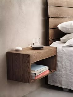 a wooden shelf with books and a cup on it next to a bed in a room