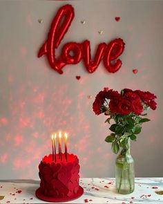 a red cake with candles on it sitting next to a vase filled with roses