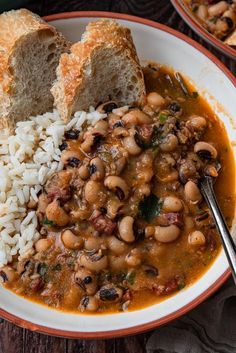 a white plate topped with beans and rice next to two slices of bread on top of a wooden table