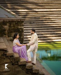 a man and woman sitting on steps near water