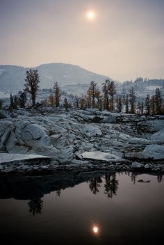 the sun is setting over some rocks and trees in the distance, with mountains in the background