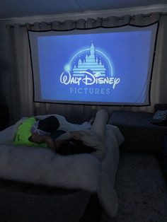 a woman laying on top of a bed in front of a large screen with the logo of walt pictures