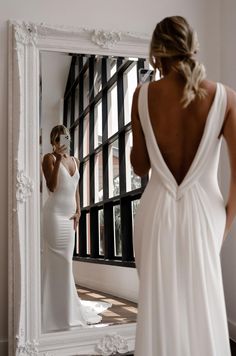 a woman in a white dress looking at her reflection in a mirror