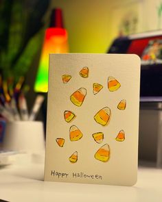 a card with candy corn on it sitting on a desk next to some pens and pencils