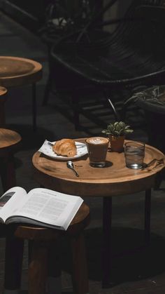 an open book sitting on top of a wooden table next to two small tables with drinks and croissants