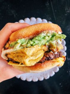 a hand holding a sandwich with meat, cheese and guacamole on it