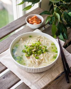 a white bowl filled with soup next to chopsticks and a potted plant