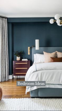 a bedroom with dark blue walls, white bedding and wooden flooring is pictured in this image