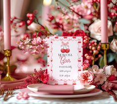 a table topped with pink flowers and candles next to a card on top of a plate