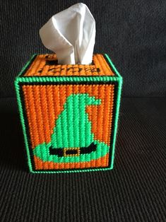 an orange and green tissue box with a witch hat on it's lid, sitting on a black surface