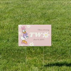 a pink sign sitting on top of a lush green grass covered field with daisies