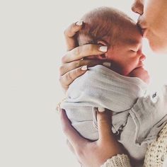 a woman holding a baby in her arms and kissing it's face with the other hand