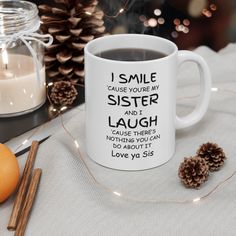 a white coffee mug sitting on top of a table next to an orange and pine cone