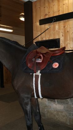 a brown horse standing next to a wooden wall with a saddle on it's back