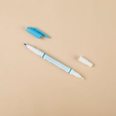 two pens sitting next to each other on top of a beige surface and one pen is blue