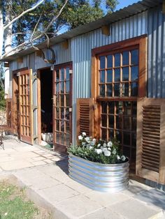 a metal planter with flowers in it on the side of a building that has wooden shutters