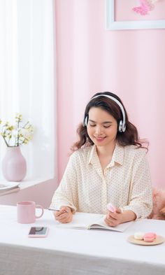 a woman wearing headphones sitting at a table with a book and cup in front of her