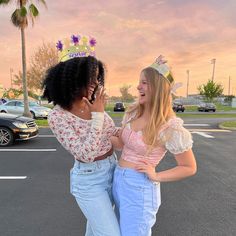 two young women standing in a parking lot talking on their cell phones while the sun is setting