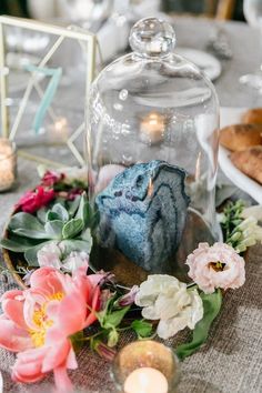 a glass clochel with flowers and candles on it sitting on top of a table