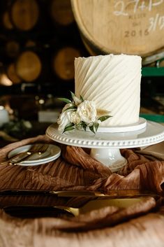 a white wedding cake sitting on top of a table next to some wine glasses and wooden barrels