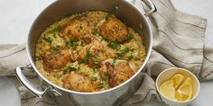 a pot filled with chicken and rice next to a small bowl of lemon wedges