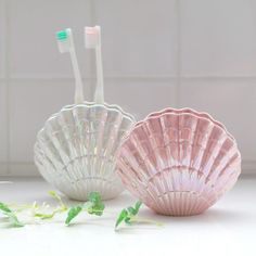 two toothbrushes sitting in shell shaped bowls on a white counter next to each other