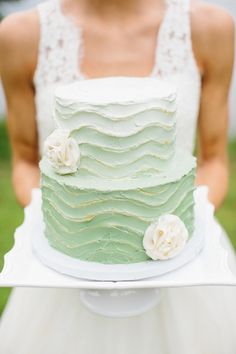 a woman holding a green cake with white flowers on the top and bottom tiers