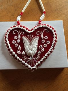 a heart - shaped box with beaded decorations on the front and side, sitting on a wooden table