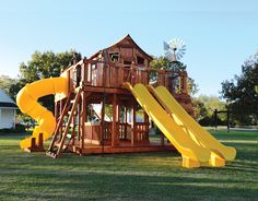 a wooden play set with yellow slides in the grass