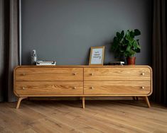 a wooden dresser sitting on top of a hard wood floor next to a potted plant