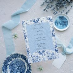 a blue and white wedding card on top of a plate next to a bowl with flowers