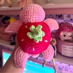 a hand holding a pink crocheted teddy bear in the shape of a strawberry