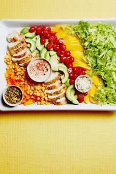 a platter filled with meat, vegetables and fruit on top of a yellow surface