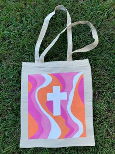 a tote bag with a cross painted on it sitting in the middle of grass