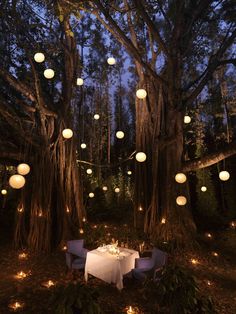 an outdoor dinner table with paper lanterns hanging from the trees in the forest at night