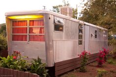 an old mobile home is sitting in the yard with flowers around it and lights on