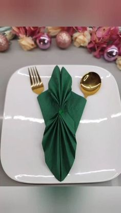 a white plate topped with a green napkin next to a gold fork and knife on top of it