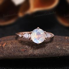 a white opal and diamond ring sitting on top of a piece of wood