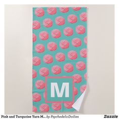 a teal towel with pink and turquoise balls of yarn on it, in front of a monogrammed background