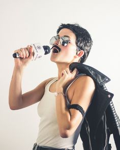 a woman in white shirt and black jacket drinking from a bottle with sunglasses on her head